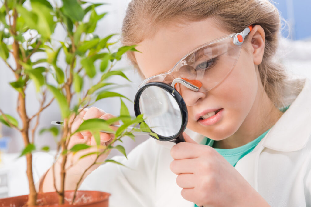 Keep your plants watered-adorable little girl in goggles with magnifying glass and plant in laboratory