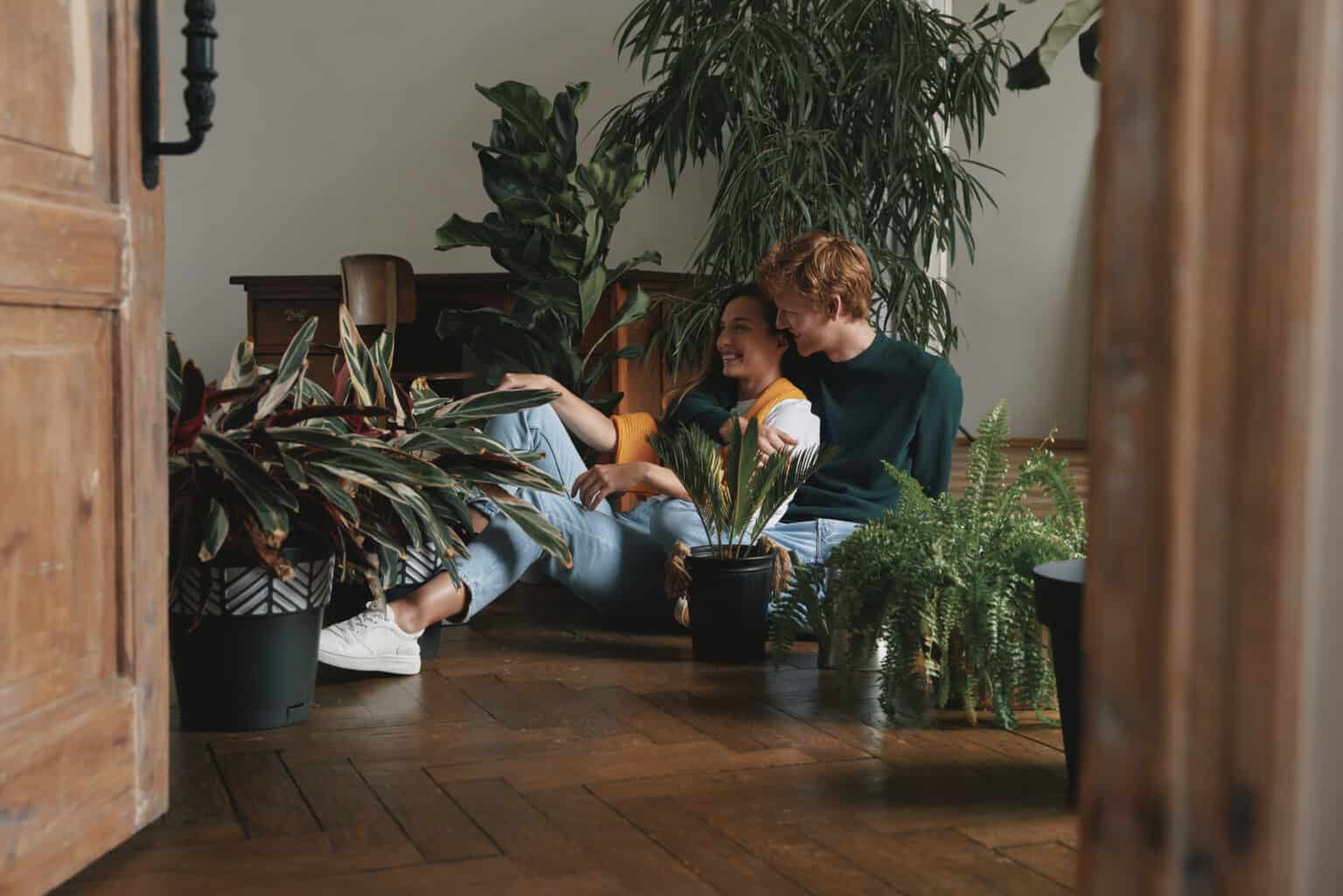 Plants For Positive Vibes: Beautiful young couple watering houseplants while sitting on the floor at home